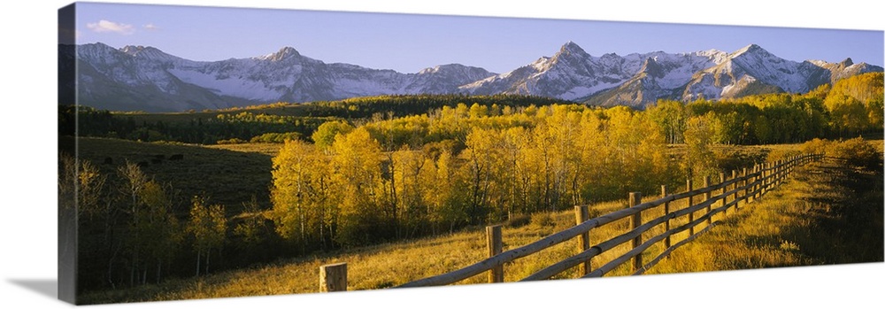 Panoramic view of the distant Rocky Mountains in the Midwestern United States, with a forest and a rustic fence in autumn.