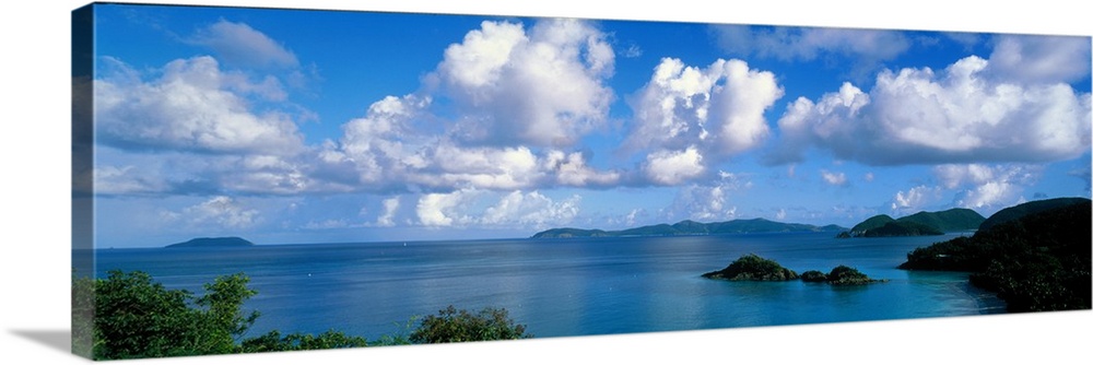 Panoramic photograph of ocean sprinkled with small grass covered islands under a cloudy sky.