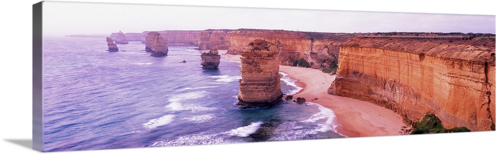 Pano of the Twelve Apostles sticking out of the Tasman Sea as the waves crash on to the sandy shore and the cliffs of shor...