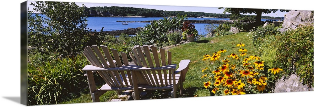 Panoramic picture taken of two chairs that sit in a garden overlooking a body of water.