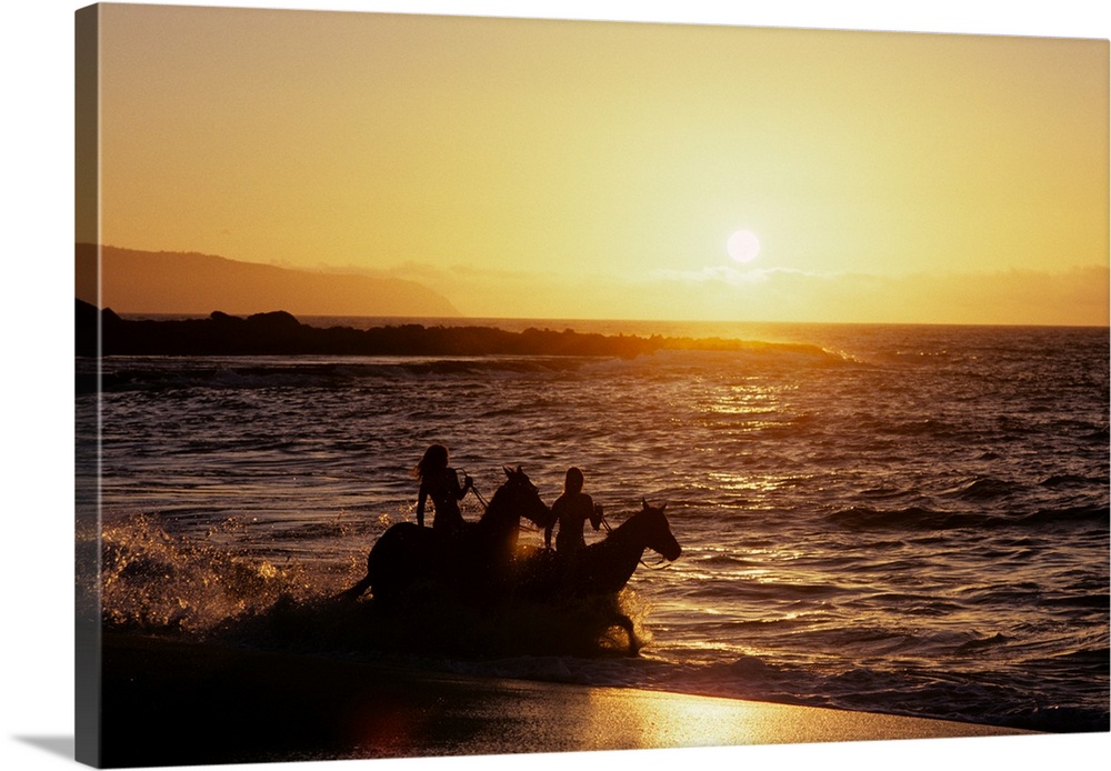 Two anonymous riders on horseback riding in surf at sunset banzai beach hawaii.