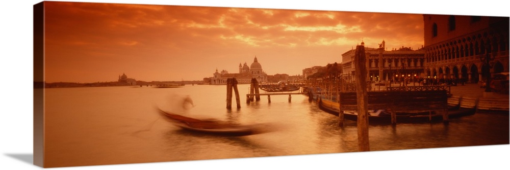 Panorama of a small Italian harbor with a blurred gondola coming into port at sunset.