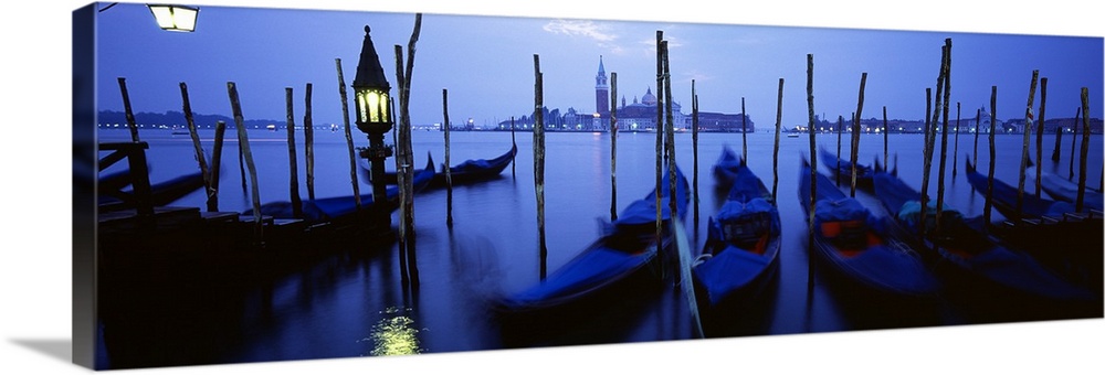 Line of gondolas moored against posts in the evening lit only by a single lamp and moonlight.