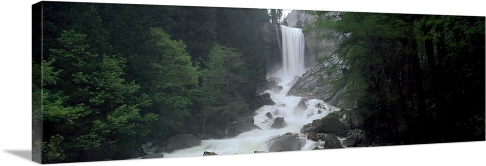 Panoramic photograph of waterfall flowing into a rocky stream lined with thick dense forest.