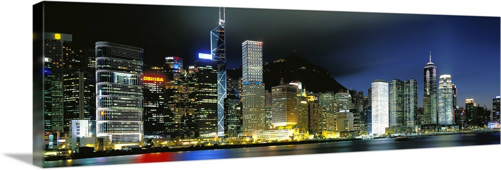 Panoramic photograph of city skyline.  The buildings are lit up in the night sky and are reflected in the waterfront.