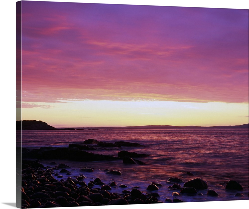This large piece is a picture taken of the sun rise off the coast of Maine. Rocks line the edge of the water and reach out...