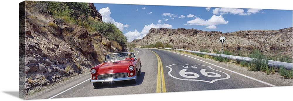 Panoramic photograph of classic car on highway winding through the mountains under a cloudy sky.