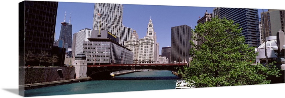 Panoramic photograph of overpass with lake below and city buildings and skyscrapers in the background under a clear sky.