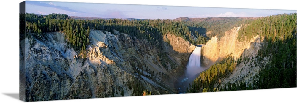 Panoramic photograph of waterfall flowing through valley surrounded by snow and tree covered mountains.