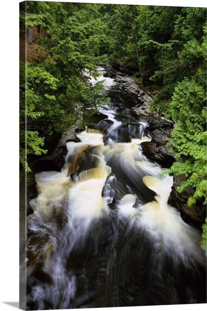 Giant, vertical, high angle photograph of water rushing through the rocky Presque Isle River, surrounded by green trees at...