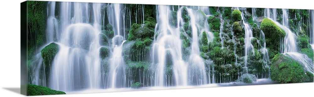 A panoramic picture taken of a massive waterfall that flows over vast green foliage.