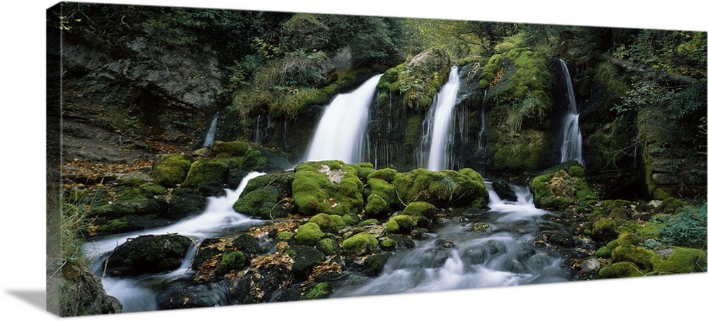Panoramic photograph of water cascading over rocks flowing into rocky moss covered stream below.
