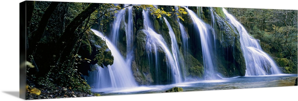 Wide angle, large wall picture of a giant waterfall surrounded by a forest in Jura, France.