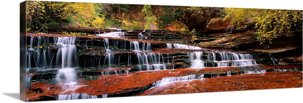 This panoramic photograph shows water trickling down the rock steps of a canyon waterfall.