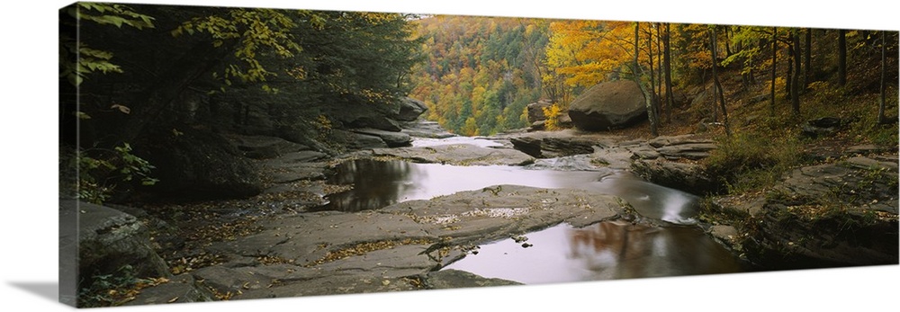 Panoramic photograph focuses on the edge of a stream filled with large rocks before it falls over a cliff and crashes agai...
