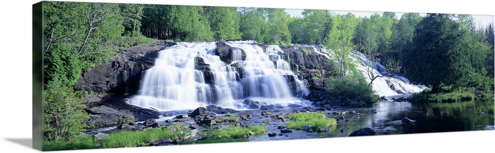 Panoramic photograph on a giant wall hanging of a wide waterfall surrounded by a lush, green forest of trees, in Michigan.