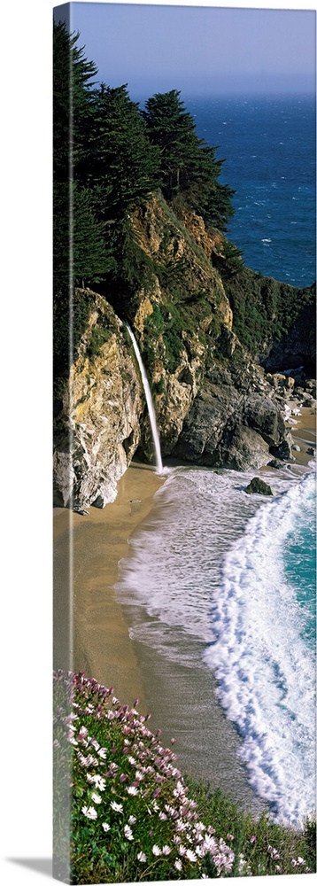 Vertical panoramic photo of a small waterfall in the rocky cliffs of the Pacific coast at low tide.