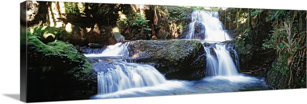 Panoramic photograph of several small waterfalls surrounded by rocky terrain and a lush, green forest in Hilo, Hawaii.