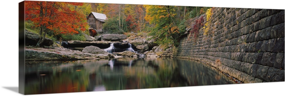 Panoramic photo of a lake with a mill in the distance surrounded by fall foliage.