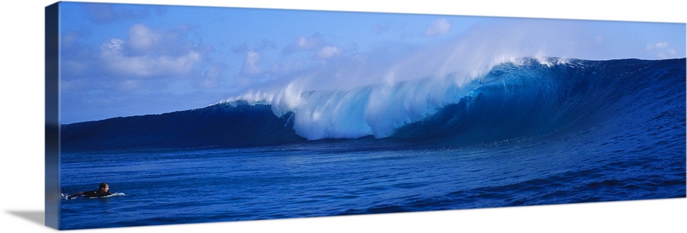 This panoramic photograph captures a curling wave collapses on itself while a surfer paddles out to sea on their board in ...