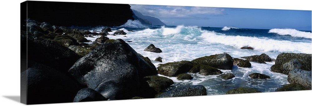 Panoramic photograph on a big canvas of waves crashing onto large rocks along the coast of Na Pali in Kauai, Hawaii.