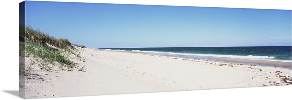 Panoramic photograph taken of the beach with the sand dunes just to the left and the ocean water coming up onto the sand.