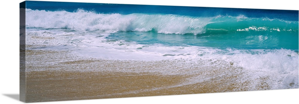 Panoramic photograph of water crashing onto the sand and being swept back out to sea.