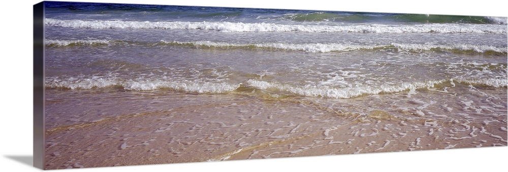 Giant, landscape photograph of small waves rolling onto the shore, covering the sand, in the Gulf of Mexico.