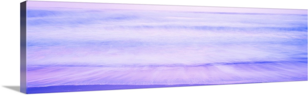 A large panoramic picture taken of waves that are about to hit the beach with a dusk like sky above and deep purple and bl...