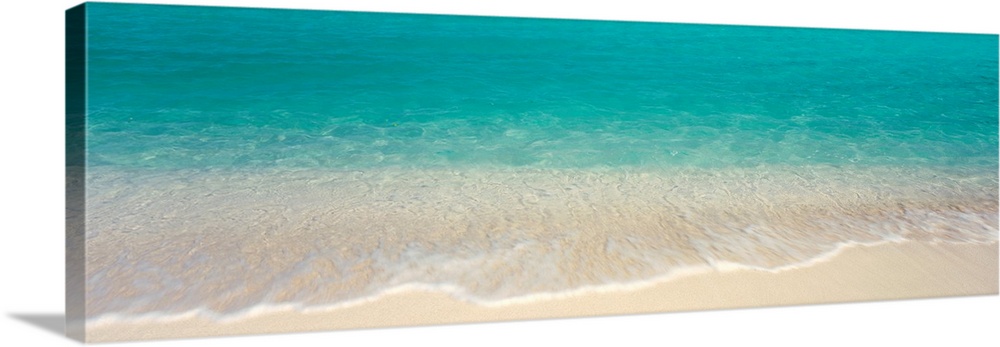 Panoramic photograph displays the clear waters of the Atlantic Ocean gently crashing into the sandy beach of an island.