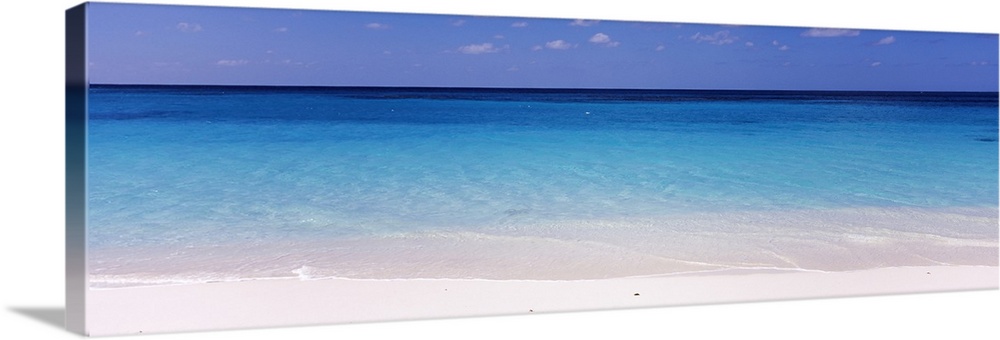 In this large panoramic photograph crystal clear water trickles onto a white sand beach in Shoal Bay Beach, Anguilla. The ...