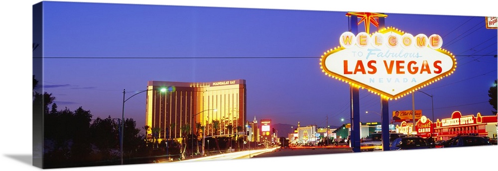 Panoramic photograph of huge neon sign in ""Sin City"" with buildings lit up in the distance at dusk.