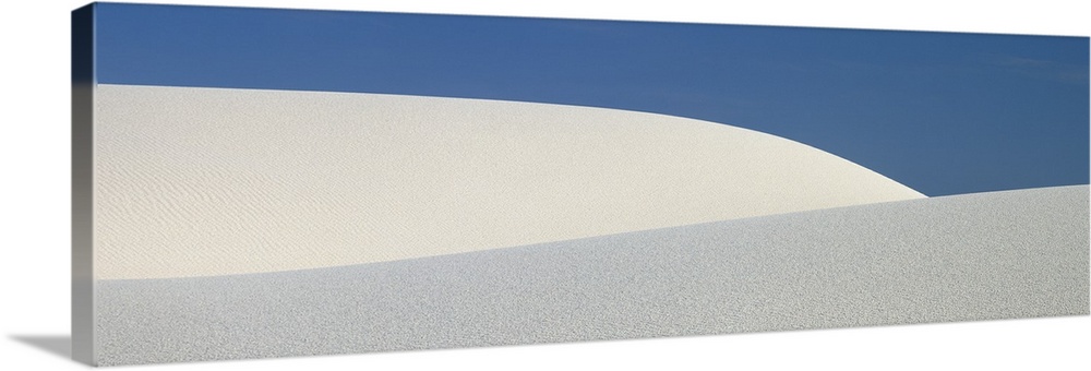 Panoramic photograph of the sloping dunes of White Sands, New Mexico, contrasting with the darker sky, creating a minimali...