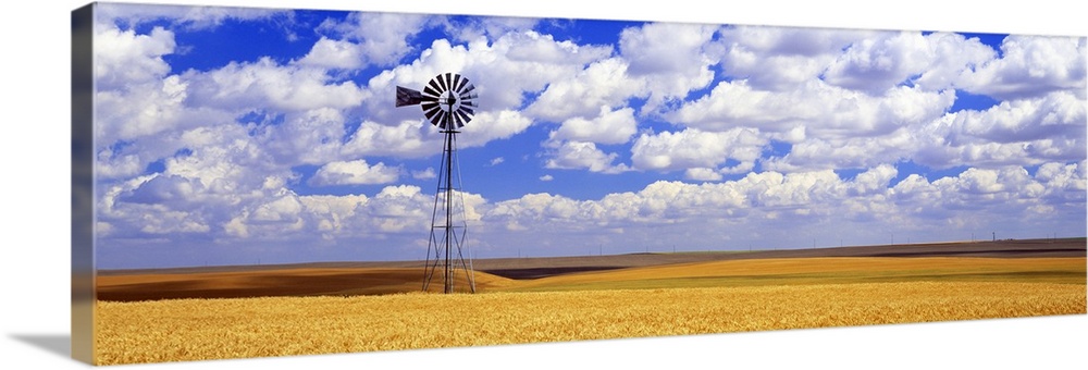 Panoramic photograph of field with tall windmill under a cloudy sky.