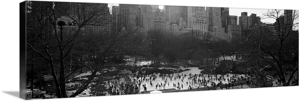 Vintage black and white photograph of a frozen pond full of ice skaters in the winter in the center of a city.