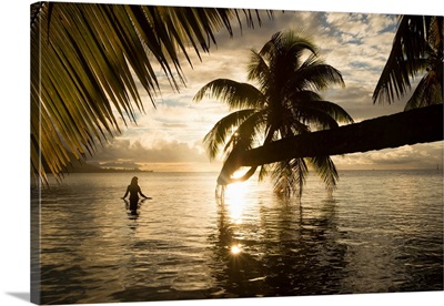 Woman standing in the Pacific Ocean at sunset, Moorea, Tahiti, French Polynesia