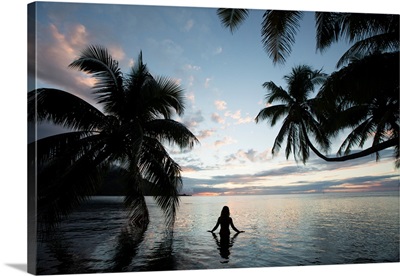 Woman standing in the Pacific Ocean at sunset, Moorea, Tahiti, French Polynesia