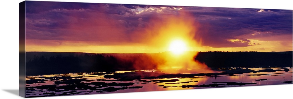 Wide angle shot of the sun setting over Yellowstone as steam billows off the water below.