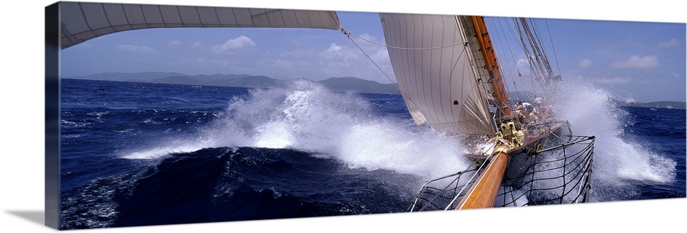 Large, horizontal photograph of two yachts racing in rough waves of the Caribbean.  One boat is in the lead, as only part ...