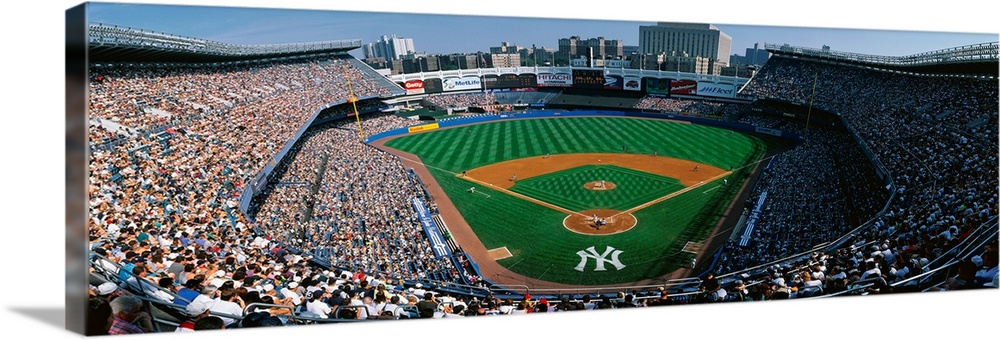 Panoramic photograph taken at Yankee Stadium in the Bronx, New York displays fans enjoying a baseball game on a sunny day....