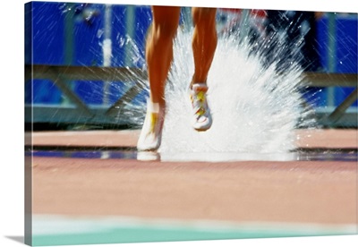 Runners' legs splashing through the water jump of a track and field steeplechase race