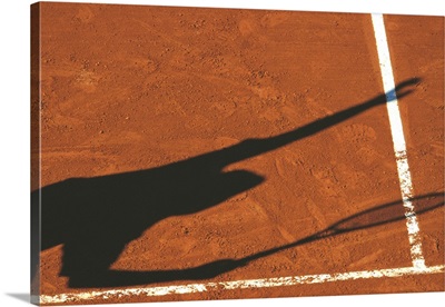 Shadow of tennis player serving on clay court