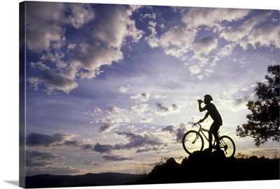 Silhouette of mountain biker drinking at the summit during sunset