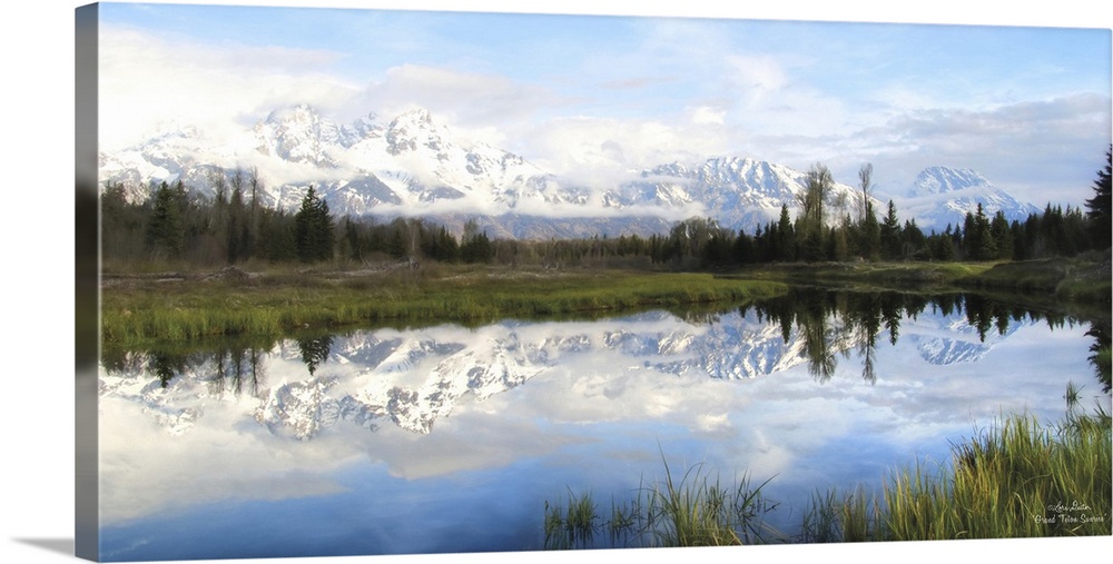 Panoramic photo of the Grand Teton mountains in the morning, reflected in the lake below.