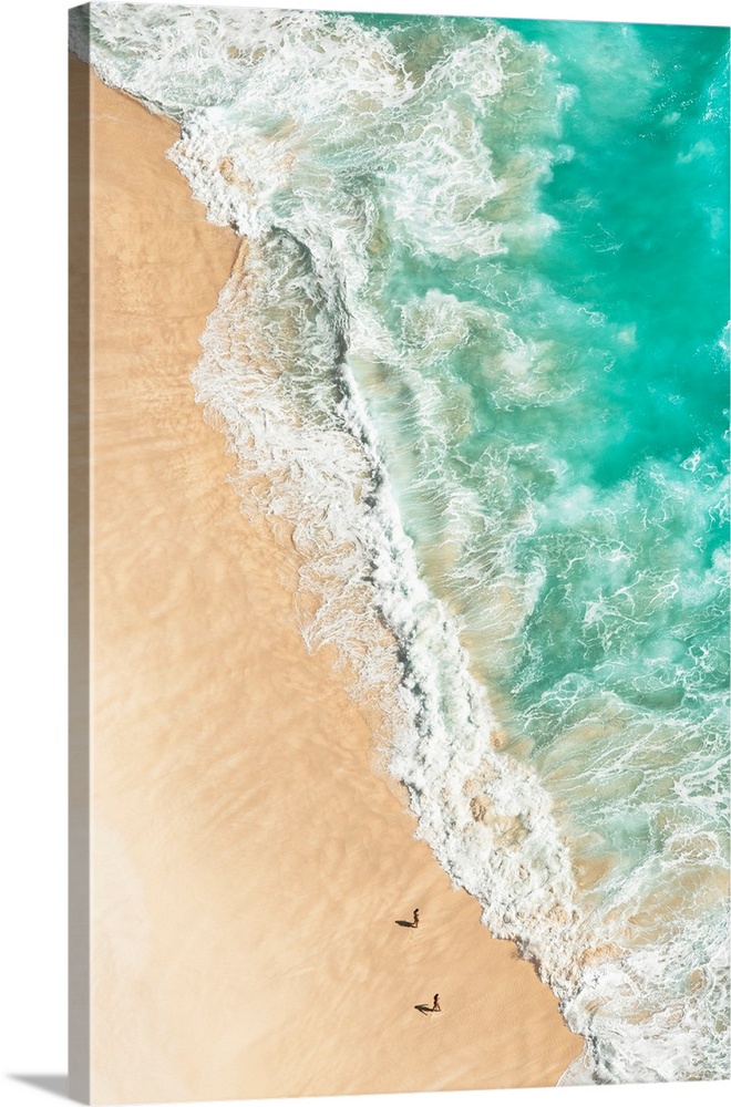 A stunning overhead aerial photograph of bright turquoise waves crashing onto a sandy beach wth two figures walking in the...