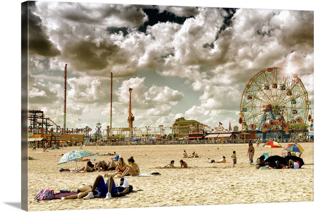 Photo of dramatic clouds over the sandy beach of Coney Island with carnival rides in the background.