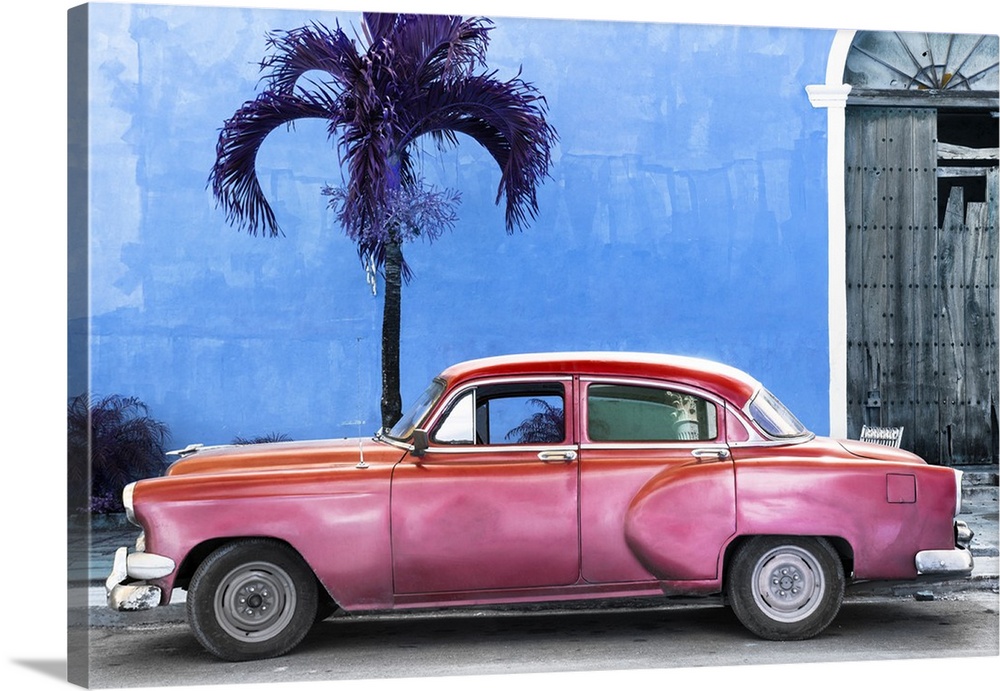 Photograph of a pink vintage car parked outside of a blue building with a palm tree.