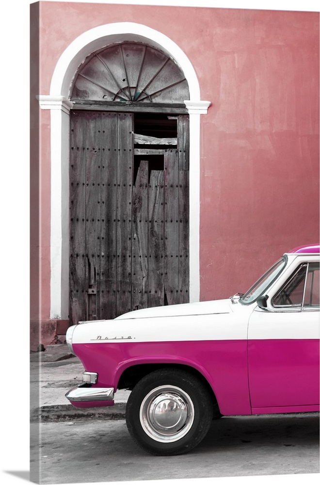 Photograph of the front of a vintage pink and white car outside of a pink building with a broken wooden door.