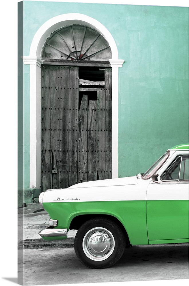 Photograph of the front of a vintage green and white car outside of a green building with a broken wooden door.