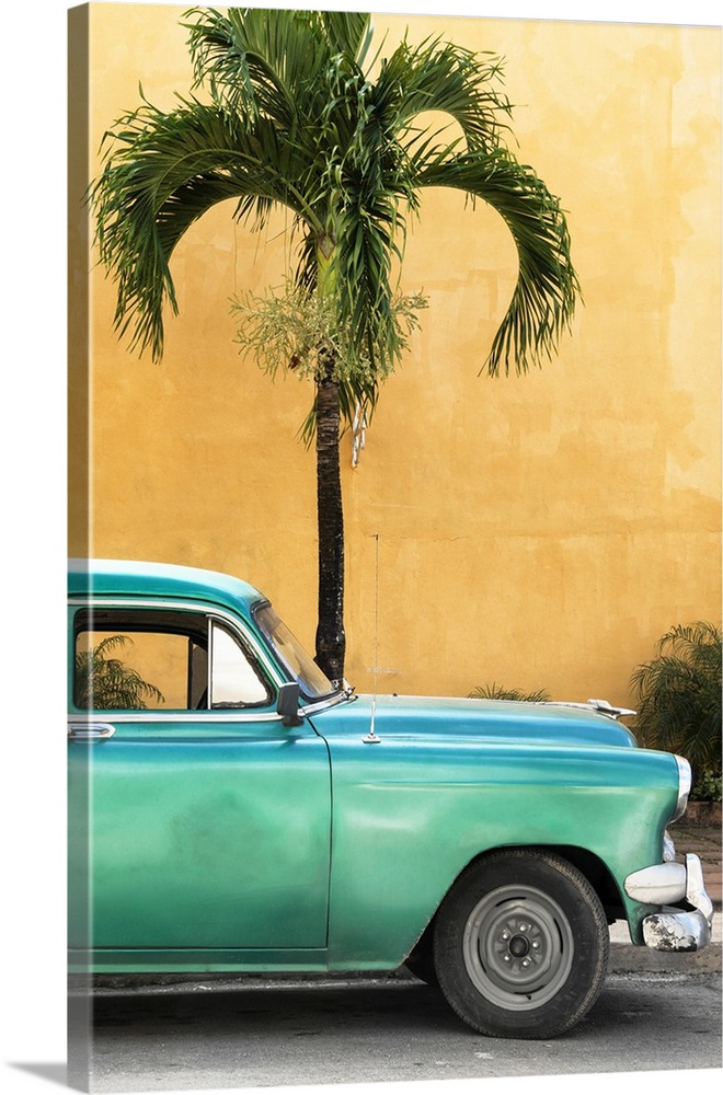 Photograph of the front half of a vintage green car in front of a palm tree and an orange wall in Havana.